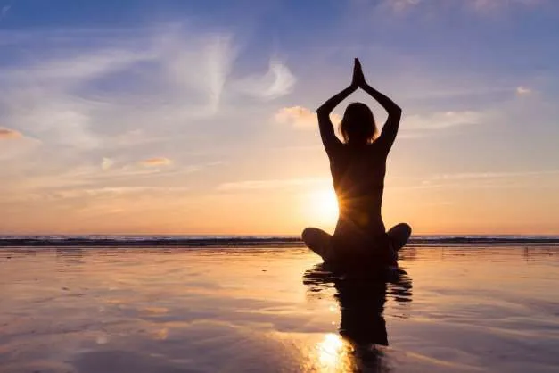 personne faisant du yoga en position du lotus, sur la plage au coucher du soleil